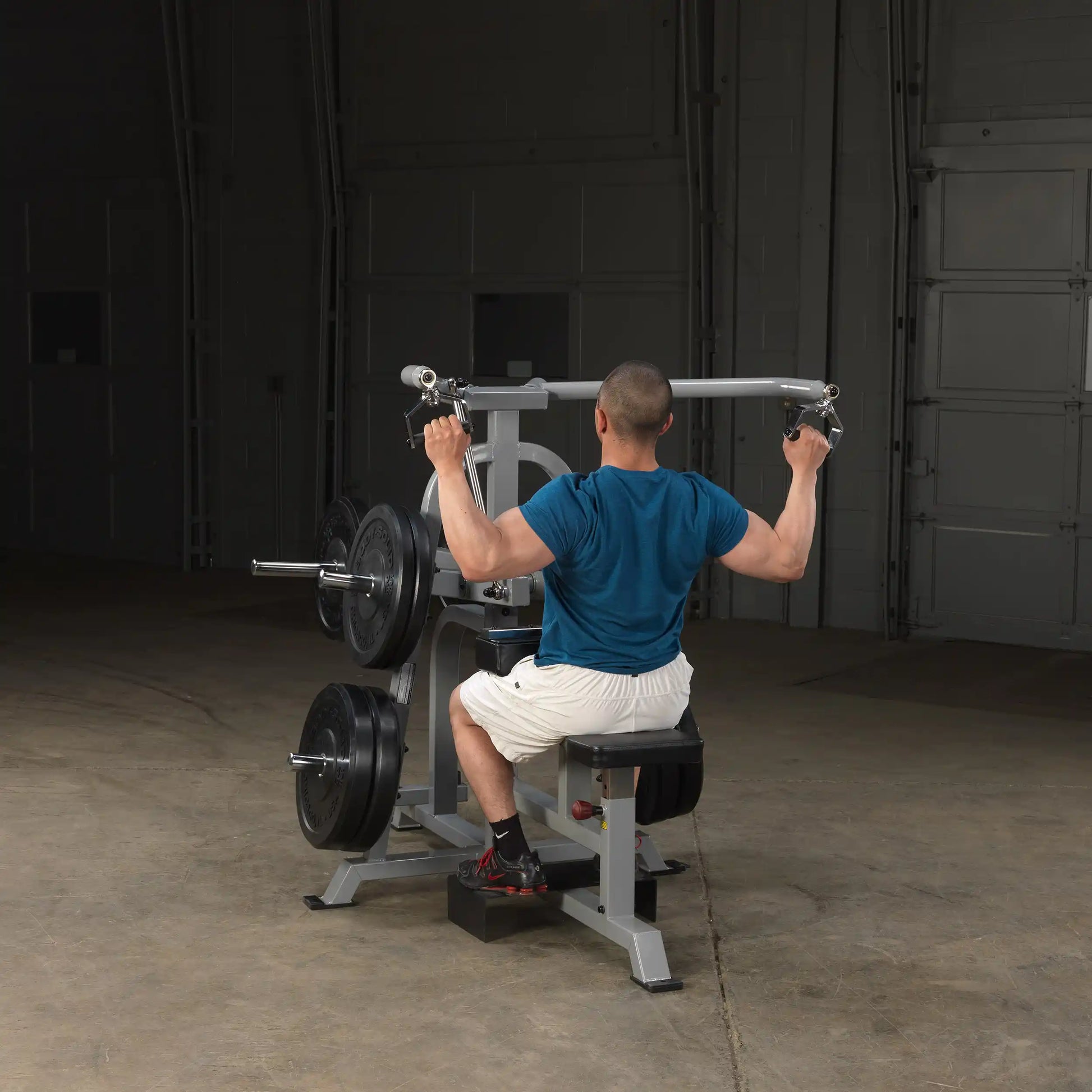 A person using the Body-Solid Pro ClubLine Leverage Lat Pulldown Machine LVLA, seated and pulling the handles down, in a gym setting.