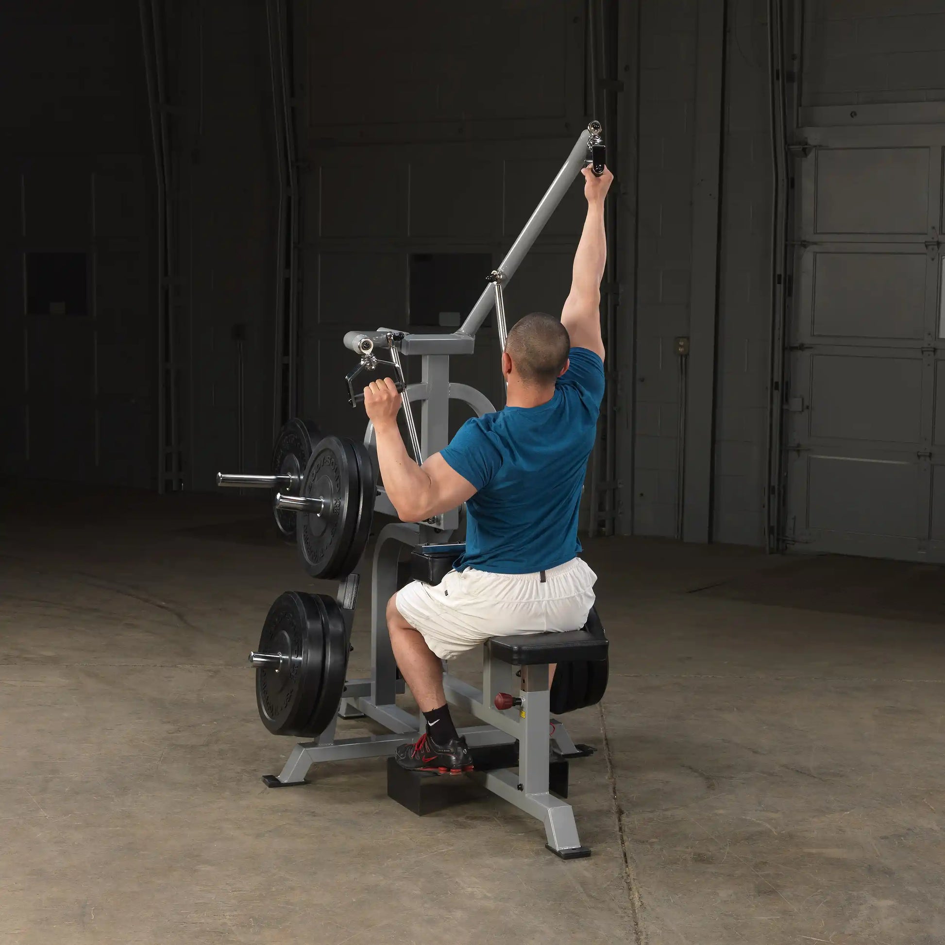 A person using the Body-Solid Pro ClubLine Leverage Lat Pulldown Machine LVLA, performing a lat pulldown exercise while seated, with weights attached to the machine in a gym setting.