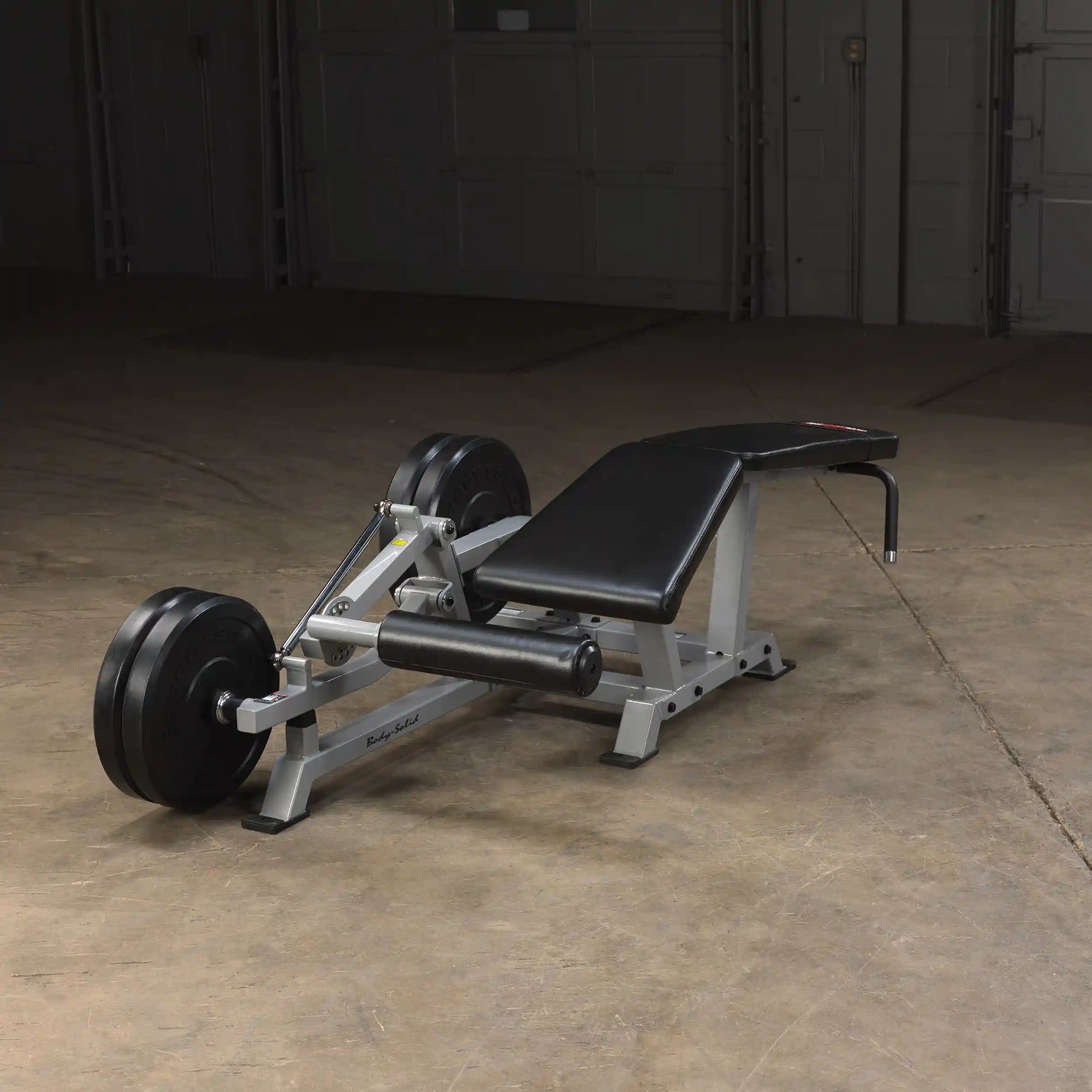 Body-Solid Pro ClubLine Leverage Leg Curl Machine LVLC positioned on a concrete floor, featuring a padded seat and adjustable components for leg workouts.
