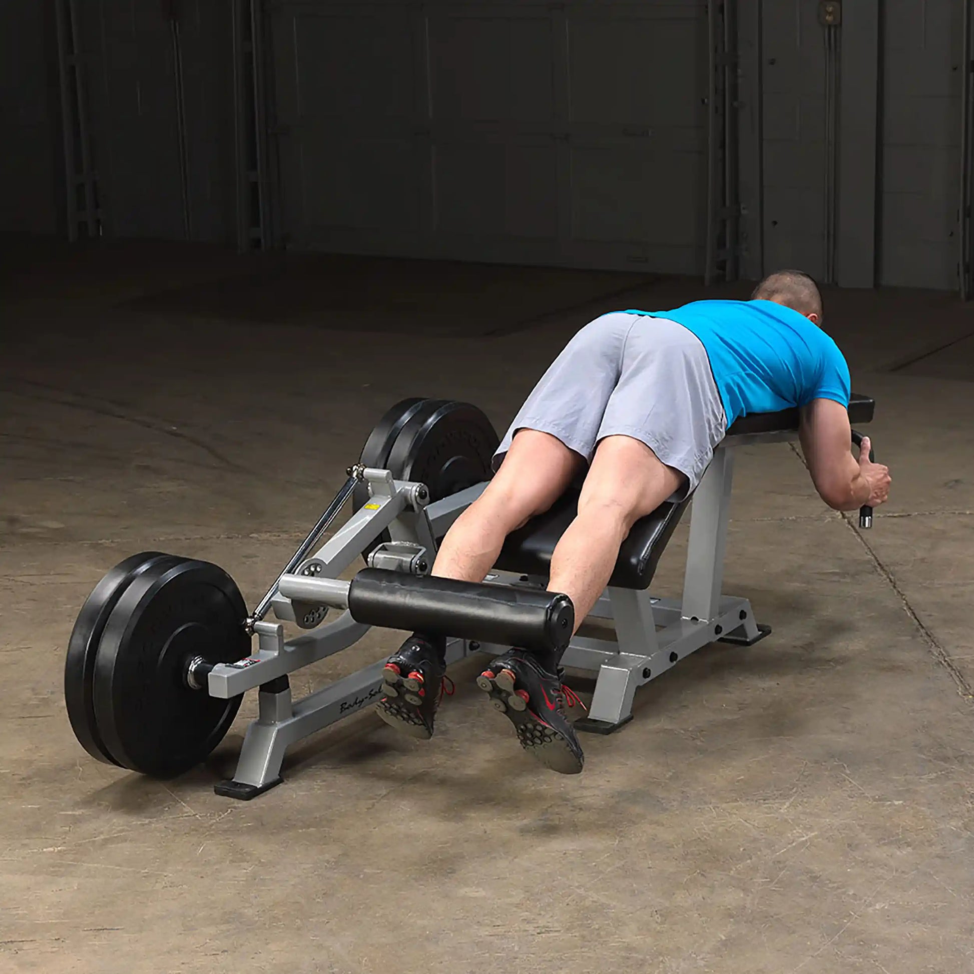 A person using the Body-Solid Pro ClubLine Leverage Leg Curl Machine LVLC, performing a leg curl exercise in a gym setting.