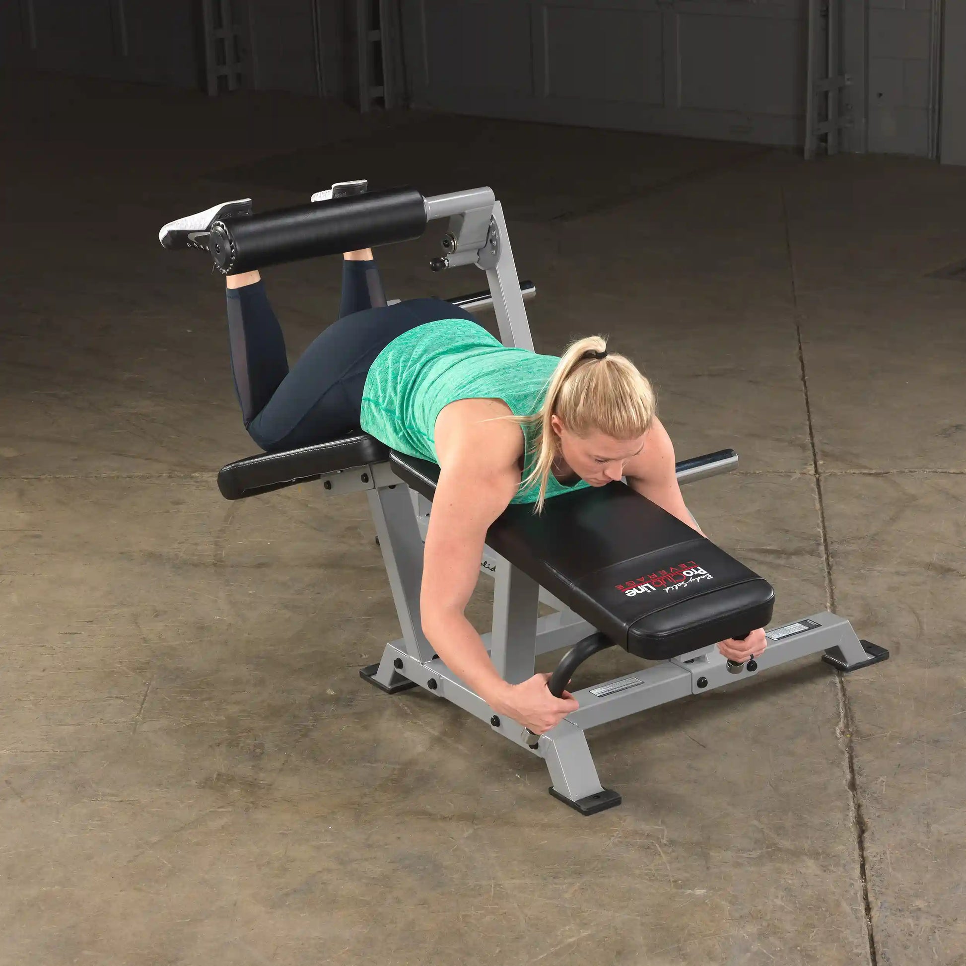 A person using the Body-Solid Pro ClubLine Leverage Leg Curl Machine LVLC in a gym setting, performing leg curls while lying on the machine.