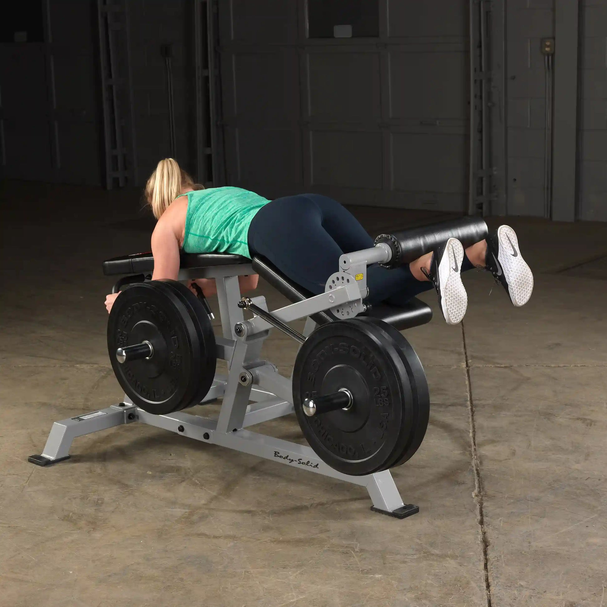 A person using the Body-Solid Pro ClubLine Leverage Leg Curl Machine LVLC, positioned on the machine with weights, performing leg curls in a gym setting.