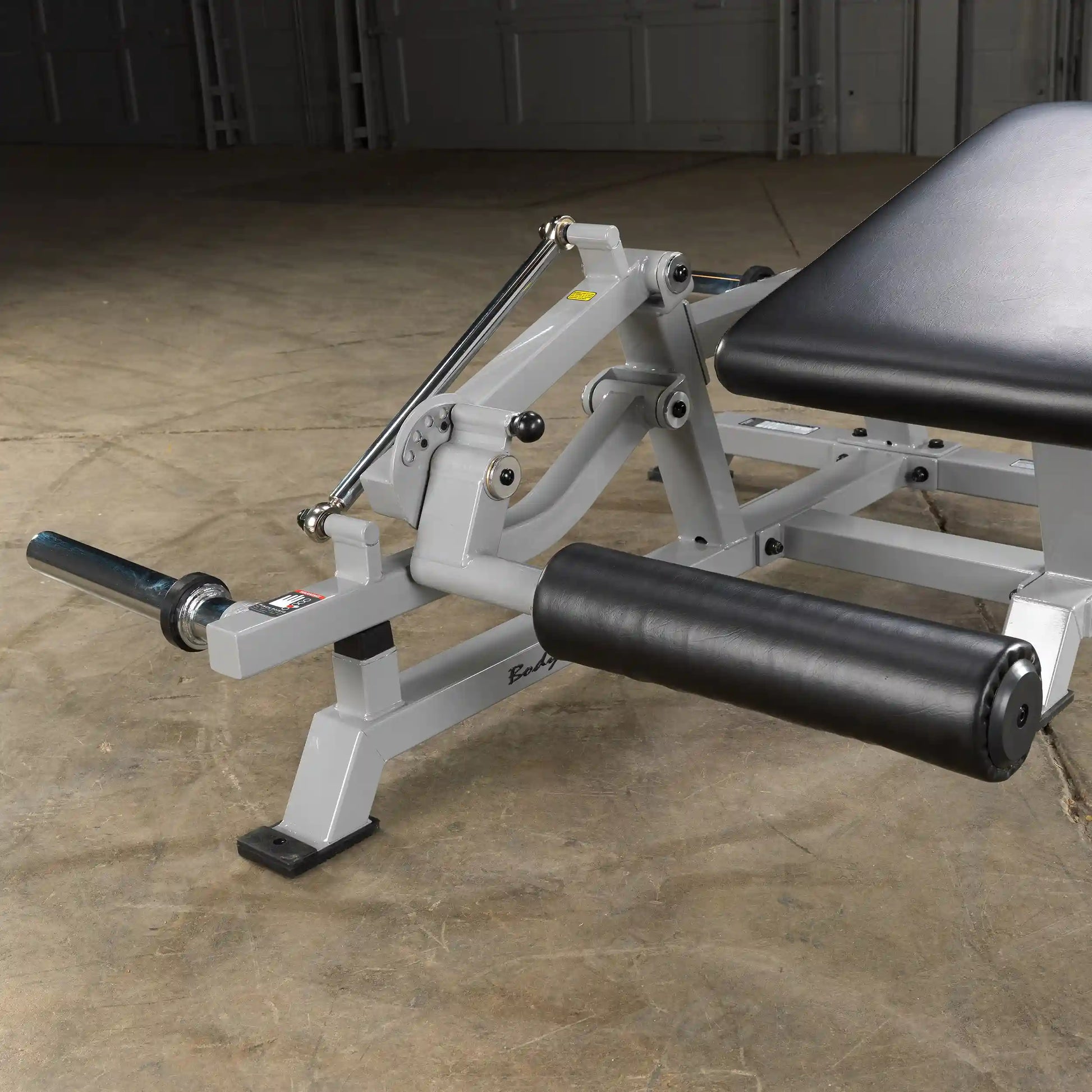 Close-up view of the Body-Solid Pro ClubLine Leverage Leg Curl Machine LVLC, featuring a padded leg support and adjustable components on a gym floor.