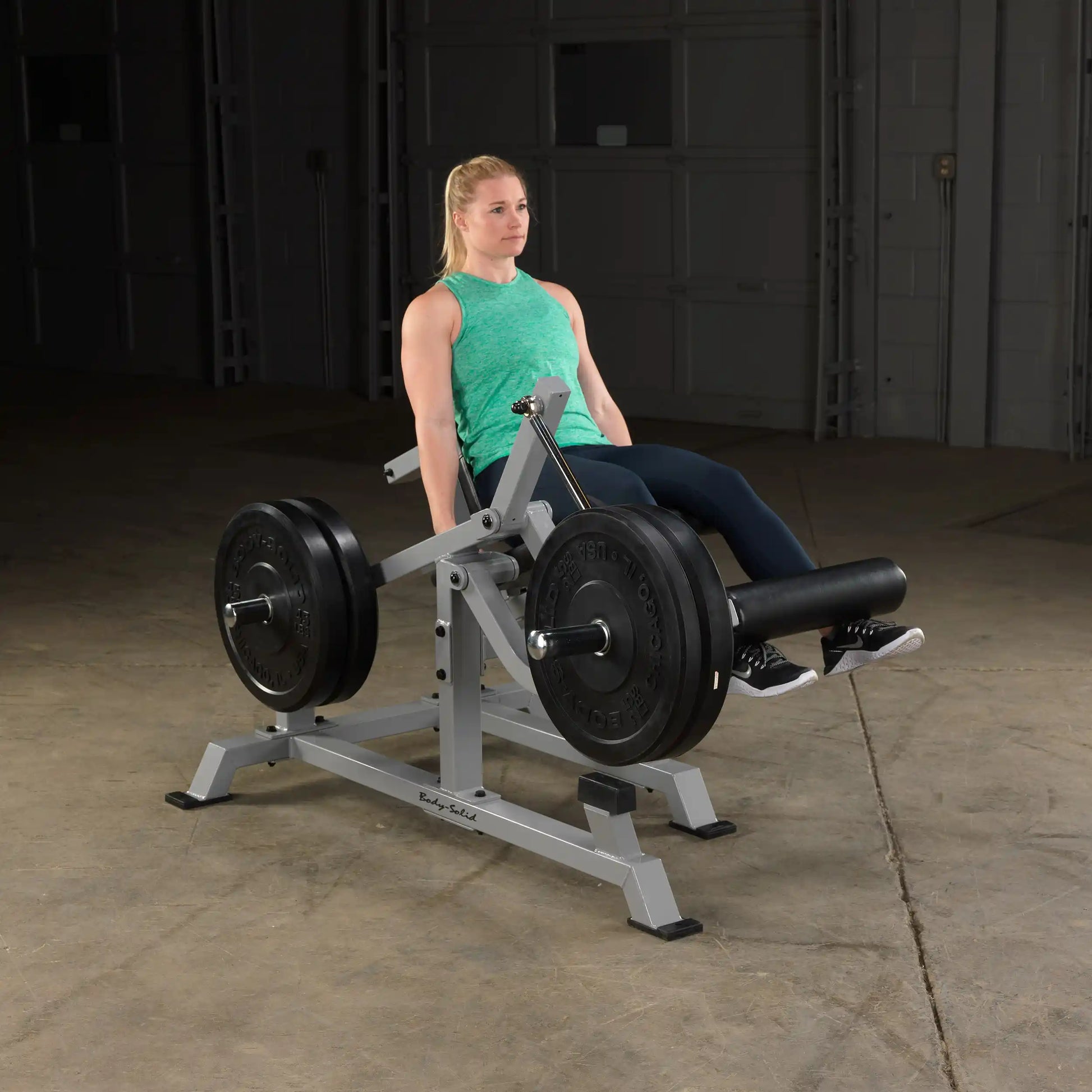 A woman using the Body-Solid Pro ClubLine Leverage Leg Extension Machine LVLE in a gym setting, demonstrating leg extension exercise with weights.