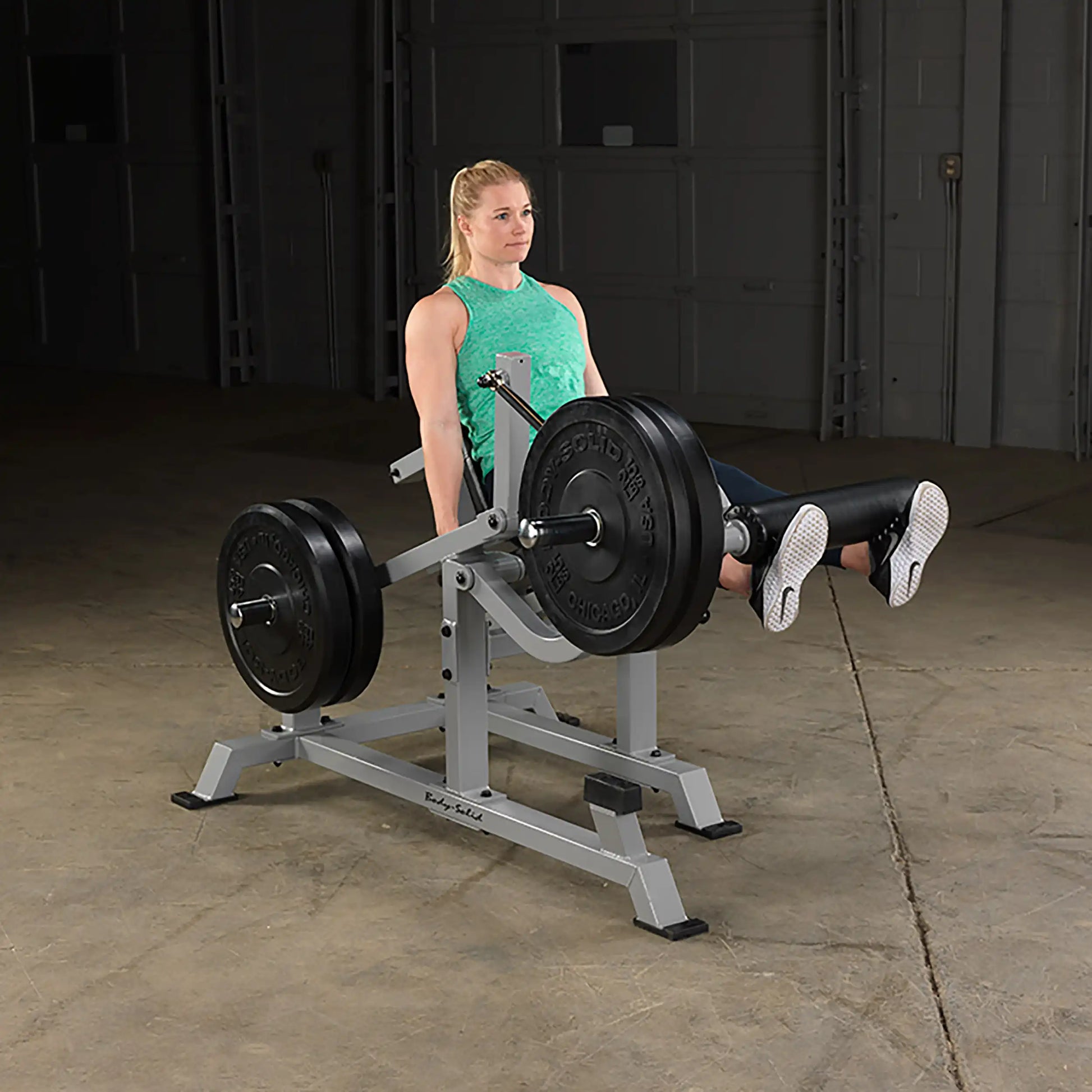 A woman using the Body-Solid Pro ClubLine Leverage Leg Extension Machine LVLE, performing leg extensions with weights in a gym setting.