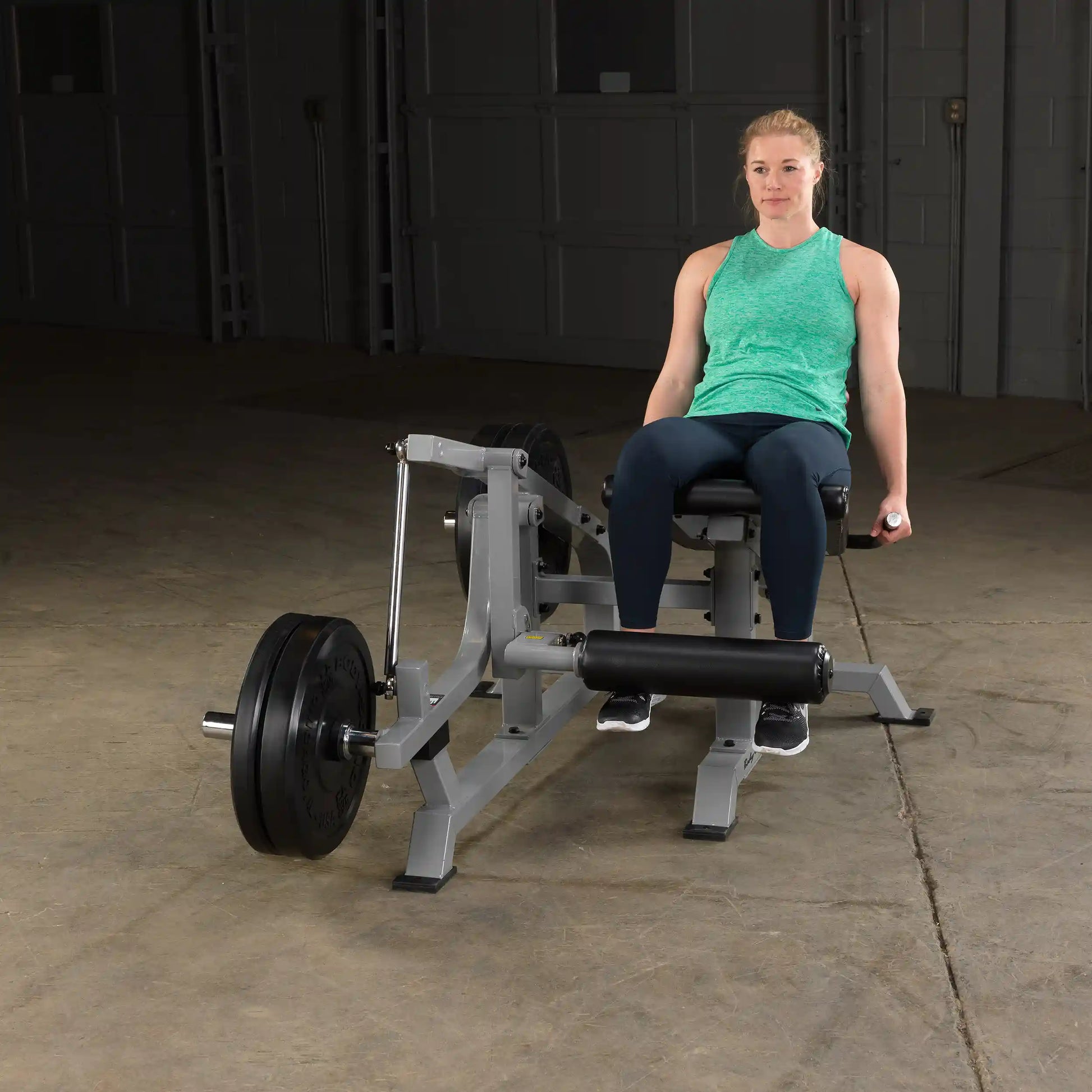 A woman using the Body-Solid Pro ClubLine Leverage Leg Extension Machine LVLE in a gym setting, demonstrating leg extension exercises.