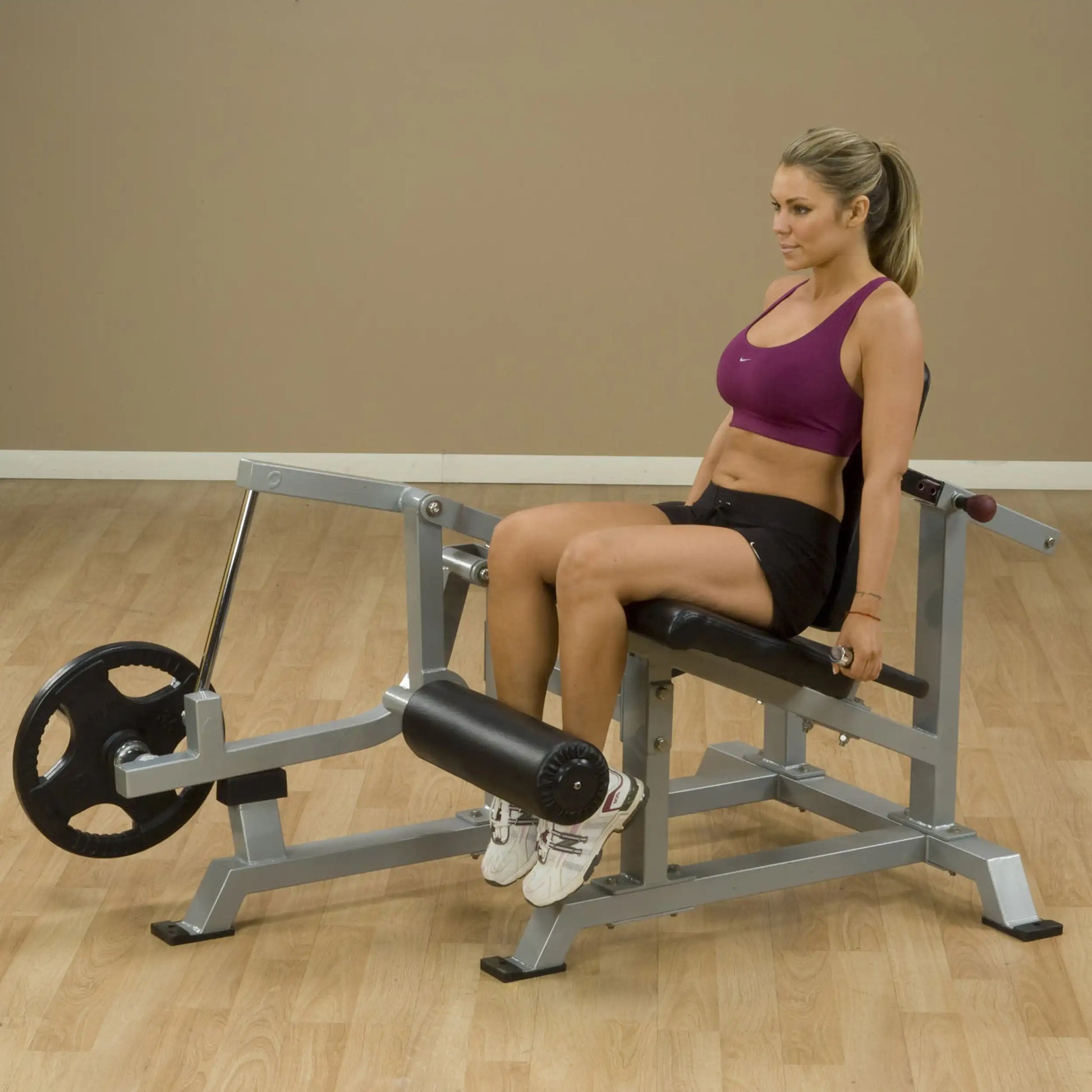 A woman using the Body-Solid Pro ClubLine Leverage Leg Extension Machine LVLE in a gym setting, performing leg extension exercises.