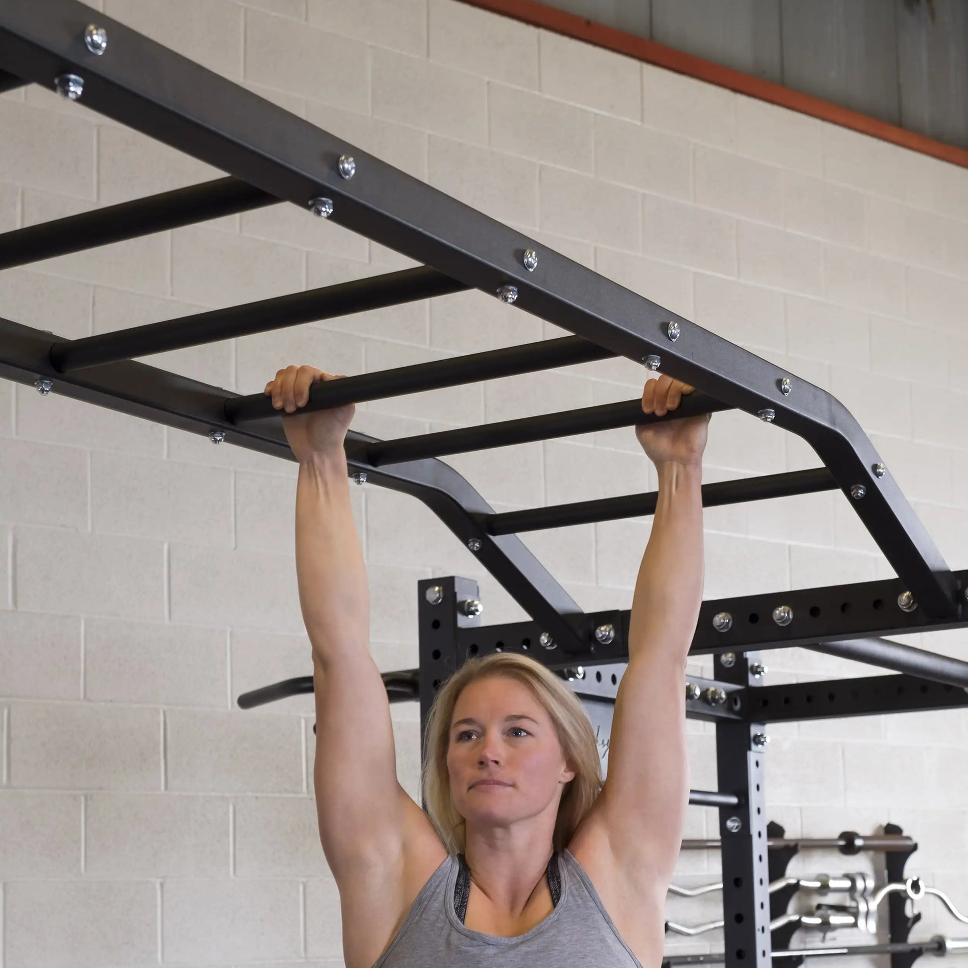 A woman demonstrating strength by hanging from the Body-Solid Pro ClubLine Monkey Bars SPRMB in a gym setting.