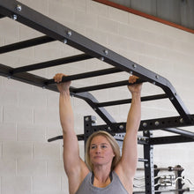 A woman demonstrating strength by hanging from the Body-Solid Pro ClubLine Monkey Bars SPRMB in a gym setting.