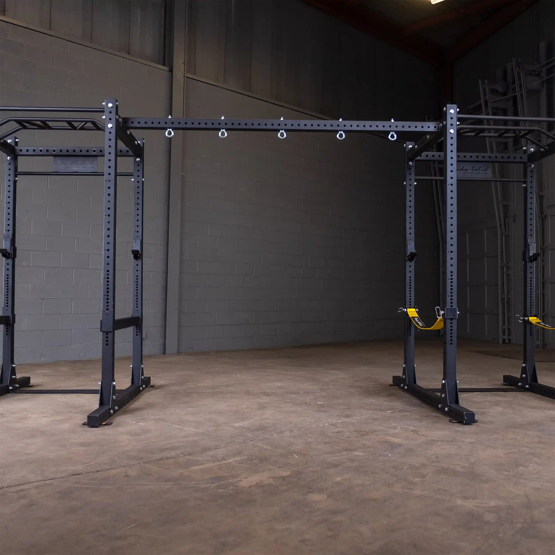 Body-Solid Pro ClubLine Power Rack Connecting Bar SPRACB set up in a spacious room with gray brick walls and wooden flooring.