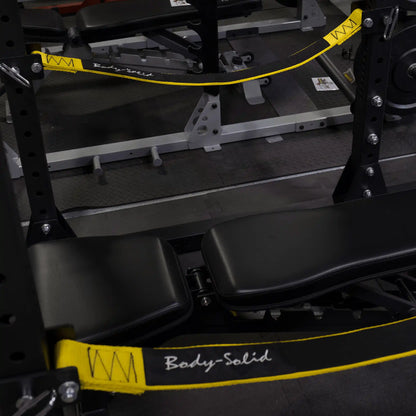Close-up of the Body-Solid Pro ClubLine Power Rack Safety Straps SPRSS with black padded benches and gym equipment in the background.