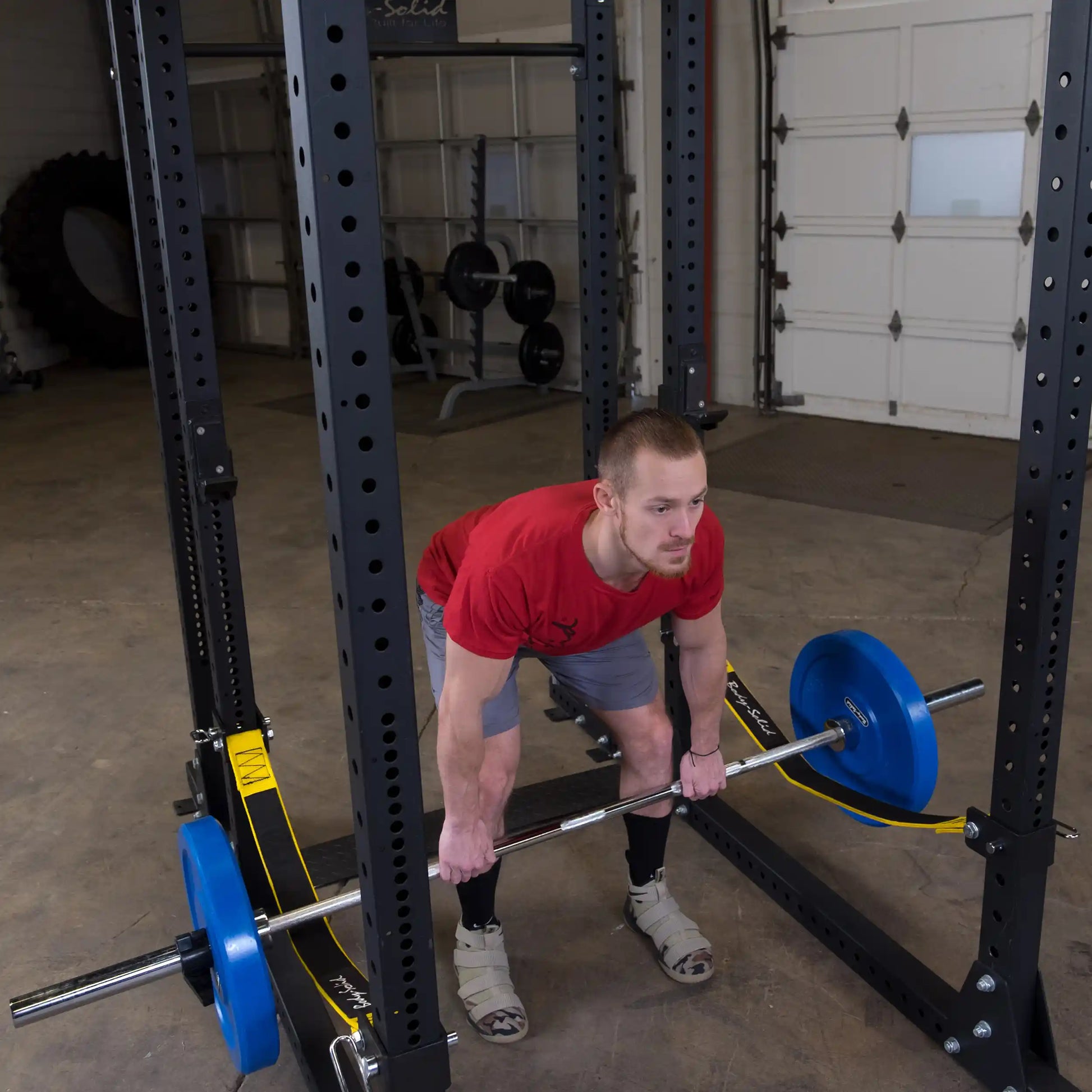 A person performing a deadlift with a barbell in a gym setting, featuring the Body-Solid Pro ClubLine Power Rack Safety Straps SPRSS in the background.