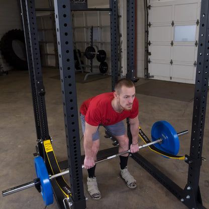 A person performing a deadlift with a barbell in a gym setting, featuring the Body-Solid Pro ClubLine Power Rack Safety Straps SPRSS in the background.