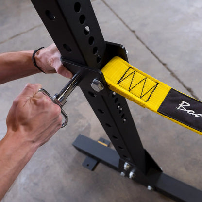 A close-up of hands adjusting the Body-Solid Pro ClubLine Power Rack Safety Straps SPRSS, featuring a yellow strap secured to a black power rack.