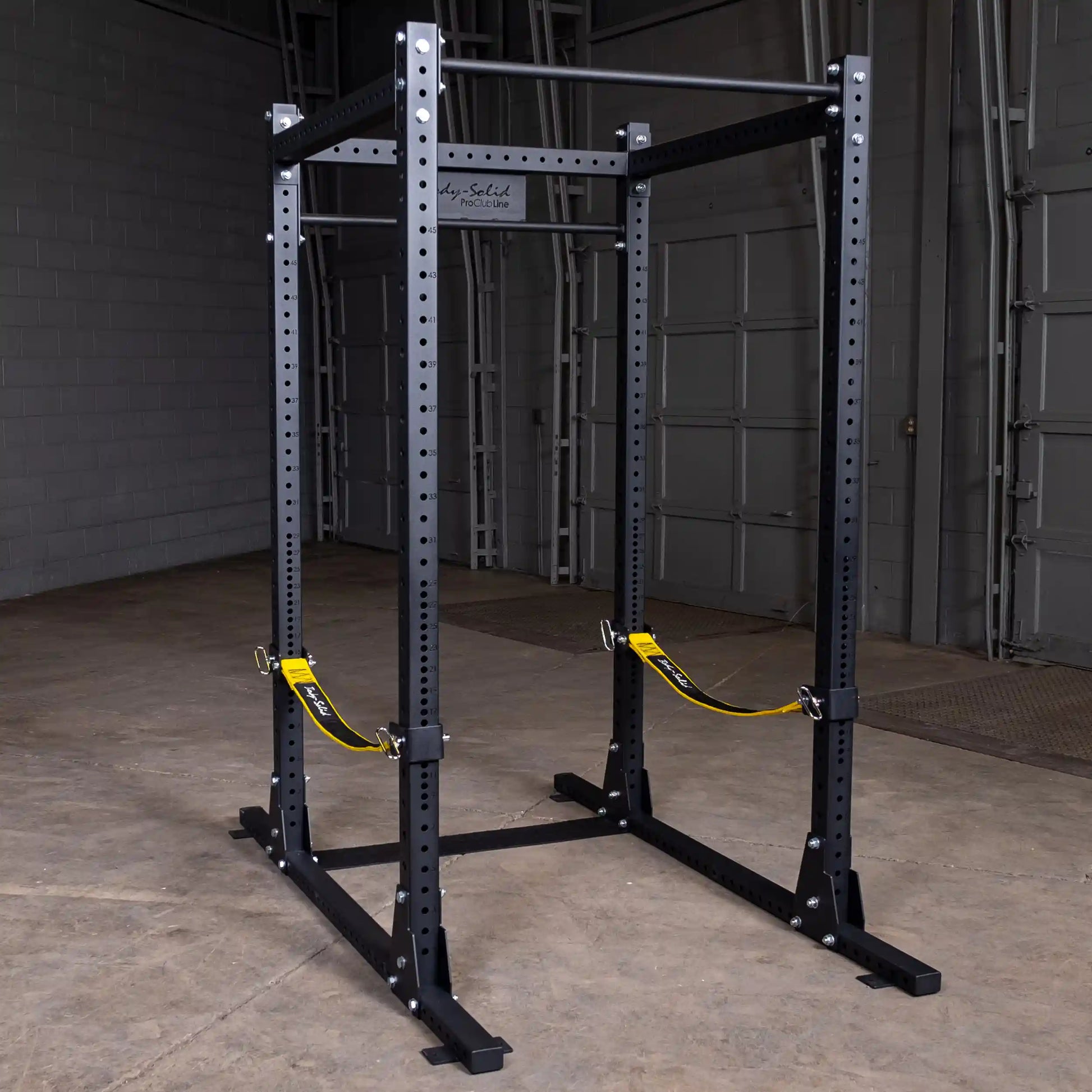 Body-Solid Pro ClubLine Power Rack with Safety Straps SPRSS set up in a gym environment, featuring a sturdy black metal frame and yellow safety straps.