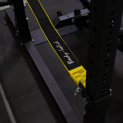 Close-up view of the Body-Solid Pro ClubLine Power Rack Safety Straps SPRSS, featuring a black and yellow design, attached to a power rack in a gym setting.