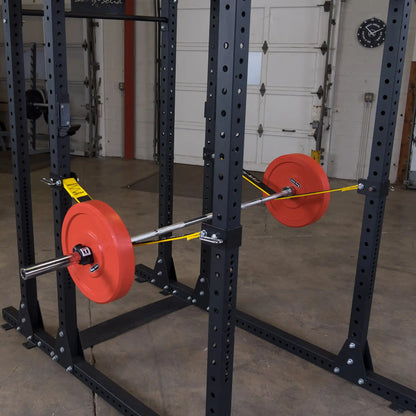 Image of a Body-Solid Pro ClubLine Power Rack featuring safety straps (SPRSS) with a barbell and weight plates positioned inside the rack, set against a gym background.