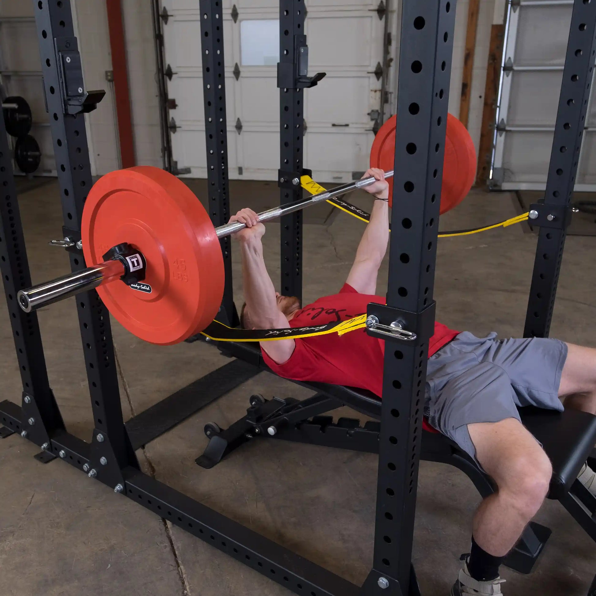 A person performing a bench press with a barbell on a Body-Solid Pro ClubLine Power Rack, featuring Safety Straps SPRSS, in a gym setting.