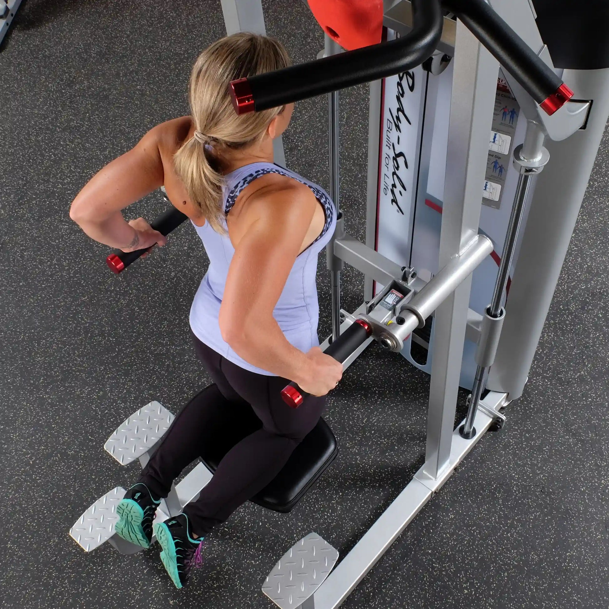 A woman using the Body-Solid Pro ClubLine Series 2 Assisted Chin & Dip Machine S2ACD, performing dips with proper form in a gym setting.