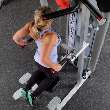 A woman using the Body-Solid Pro ClubLine Series 2 Assisted Chin & Dip Machine S2ACD, performing dips with proper form in a gym setting.