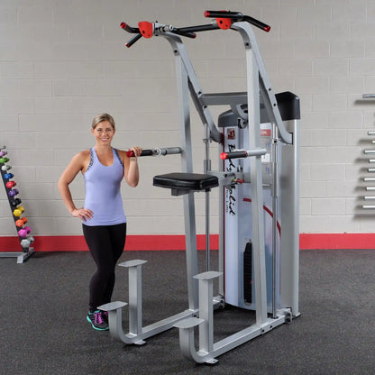 A woman stands next to the Body-Solid Pro ClubLine Series 2 Assisted Chin & Dip Machine S2ACD in a gym setting, showcasing the equipment designed for assisted chin-ups and dips.