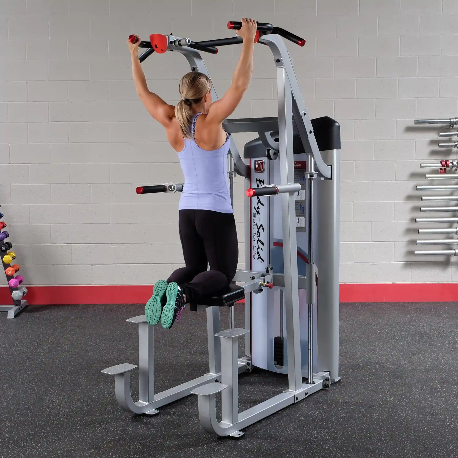 A woman using the Body-Solid Pro ClubLine Series 2 Assisted Chin & Dip Machine S2ACD in a gym setting, performing an assisted chin-up exercise.