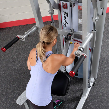 A woman adjusting the Body-Solid Pro ClubLine Series 2 Assisted Chin & Dip Machine S2ACD in a gym setting.