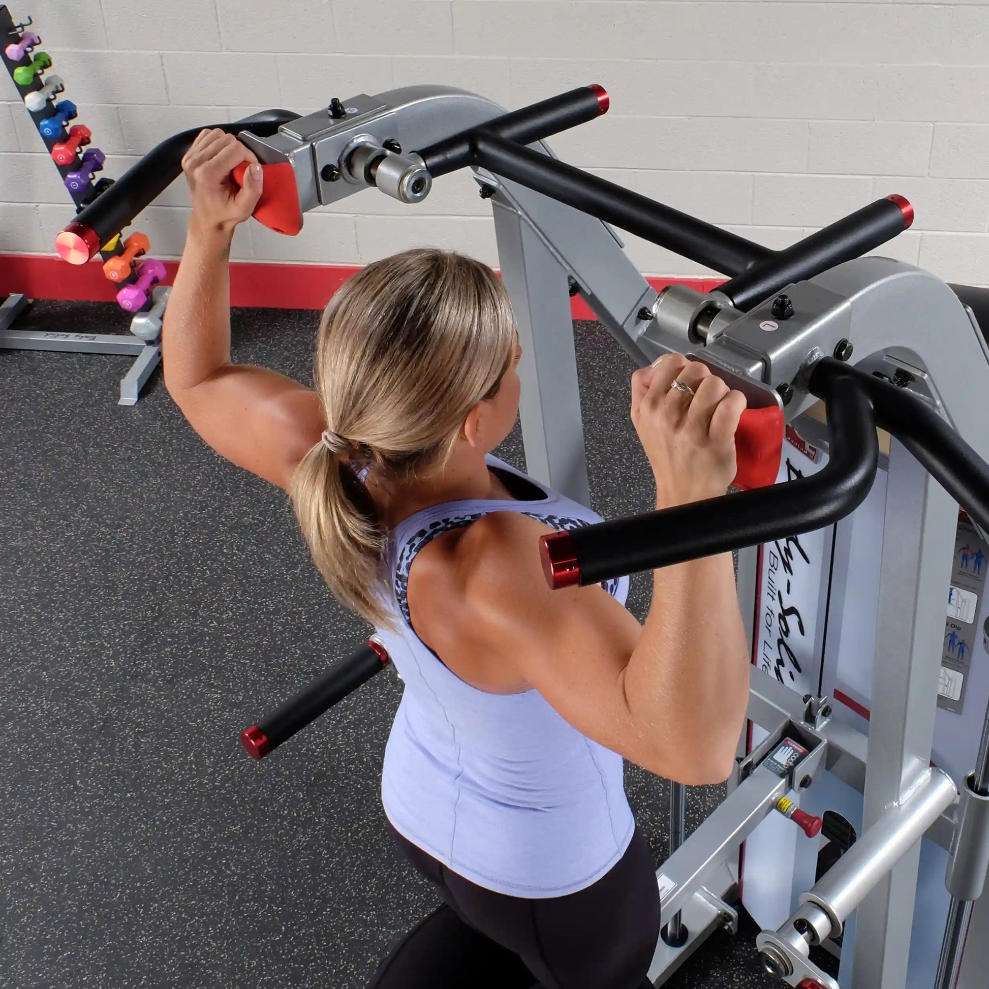 A woman using the Body-Solid Pro ClubLine Series 2 Assisted Chin & Dip Machine S2ACD in a gym setting, focusing on her upper body workout.