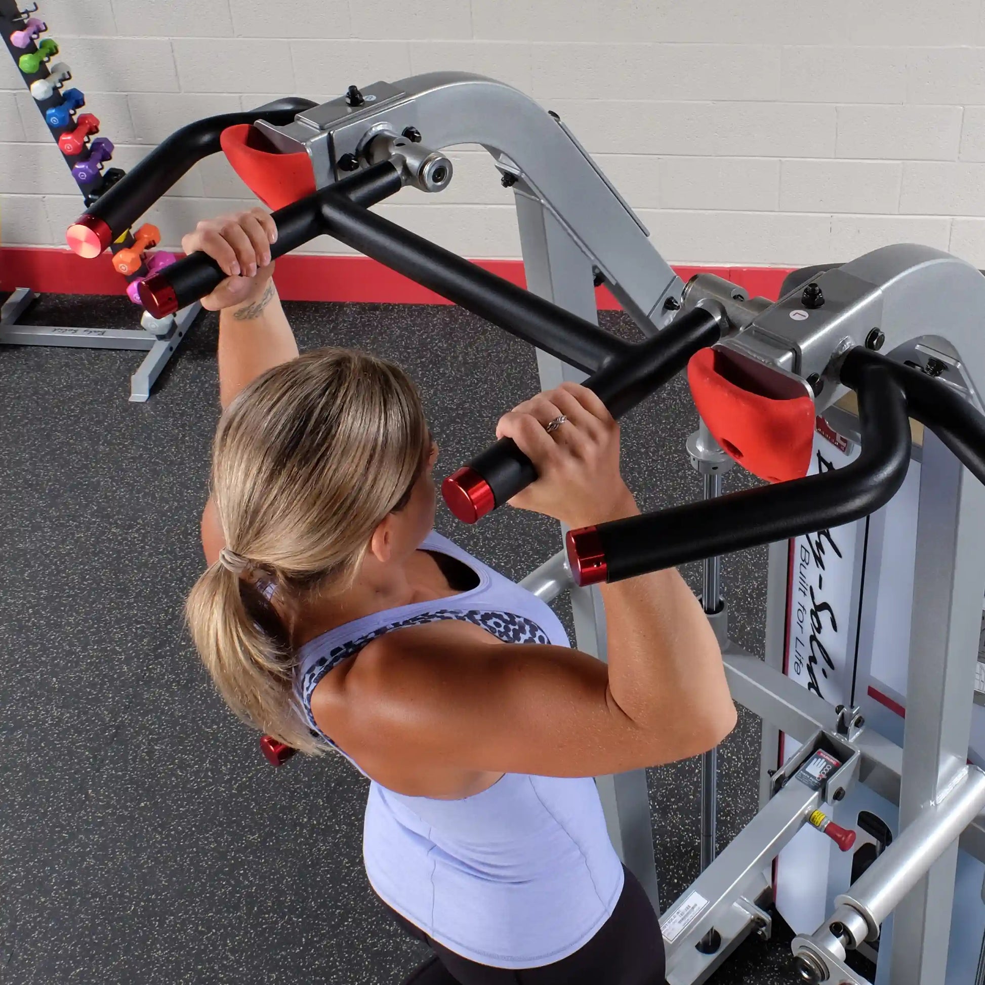A woman using the Body-Solid Pro ClubLine Series 2 Assisted Chin & Dip Machine S2ACD in a gym setting, performing an assisted chin-up exercise.