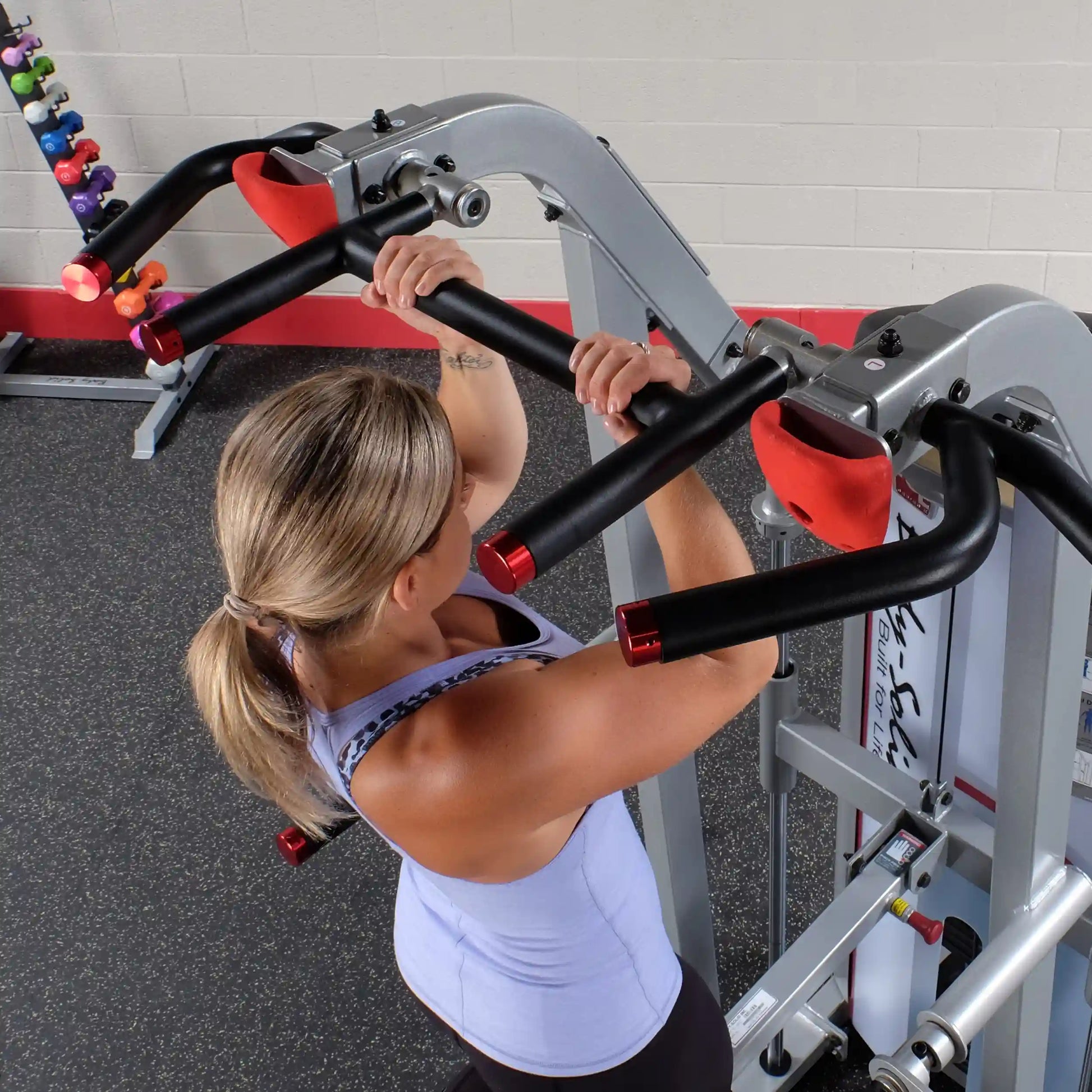 Woman performing an exercise on the Body-Solid Pro ClubLine Series 2 Assisted Chin & Dip Machine S2ACD, showcasing her grip on the handles in a gym setting.