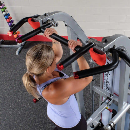 Woman performing an exercise on the Body-Solid Pro ClubLine Series 2 Assisted Chin & Dip Machine S2ACD, showcasing her grip on the handles in a gym setting.
