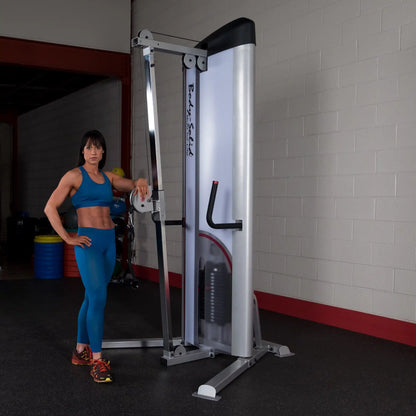 A fit woman in a blue athletic outfit poses next to the Body-Solid Pro ClubLine Series 2 Cable Column S2CC in a gym setting.