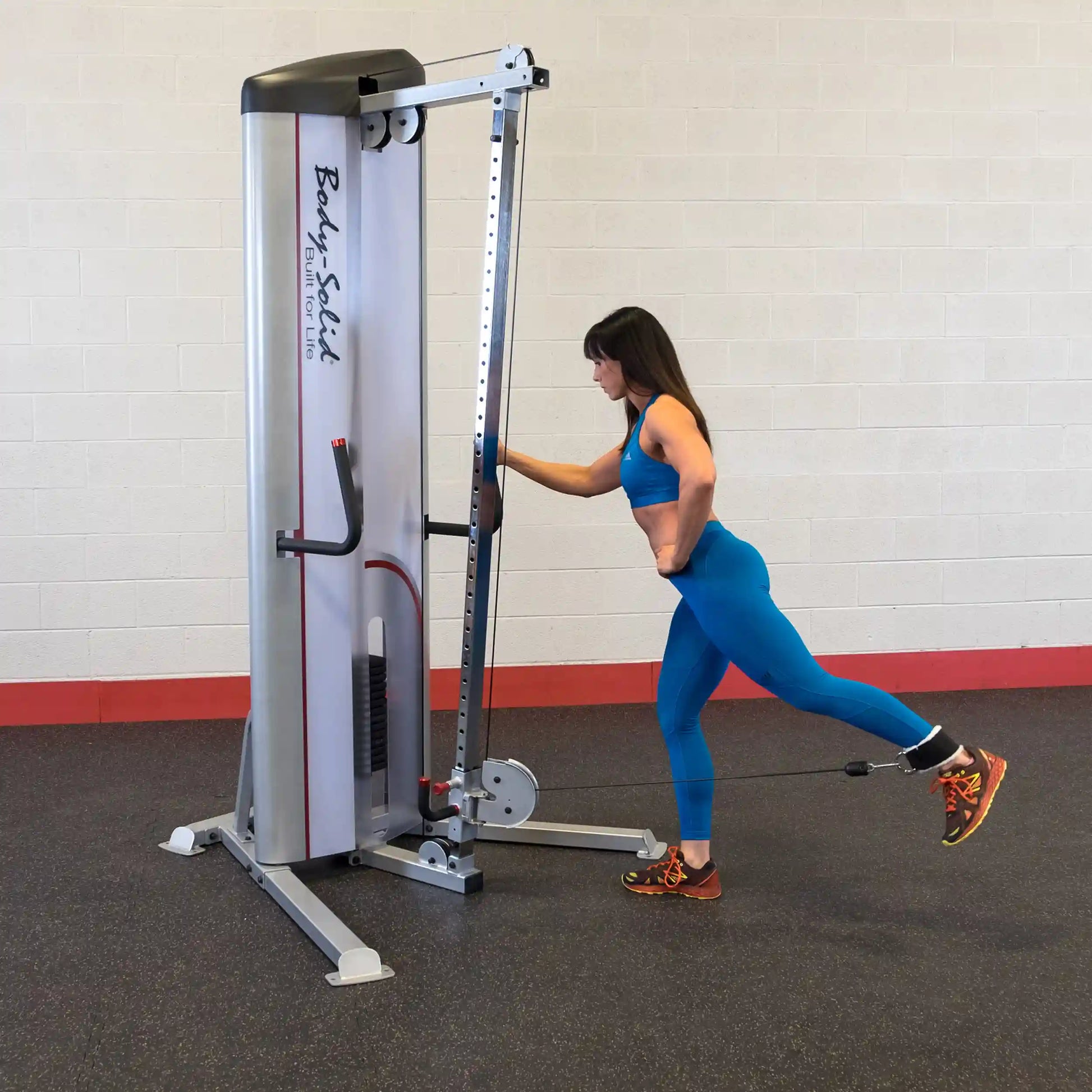 A woman in a blue workout outfit using the Body-Solid Pro ClubLine Series 2 Cable Column S2CC for resistance training, performing a leg exercise in a gym setting.