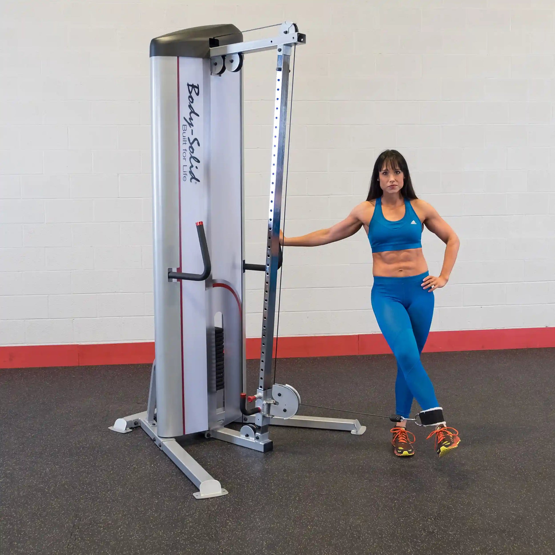 A woman in athletic wear stands next to the Body-Solid Pro ClubLine Series 2 Cable Column S2CC, showcasing the fitness equipment in a gym setting.