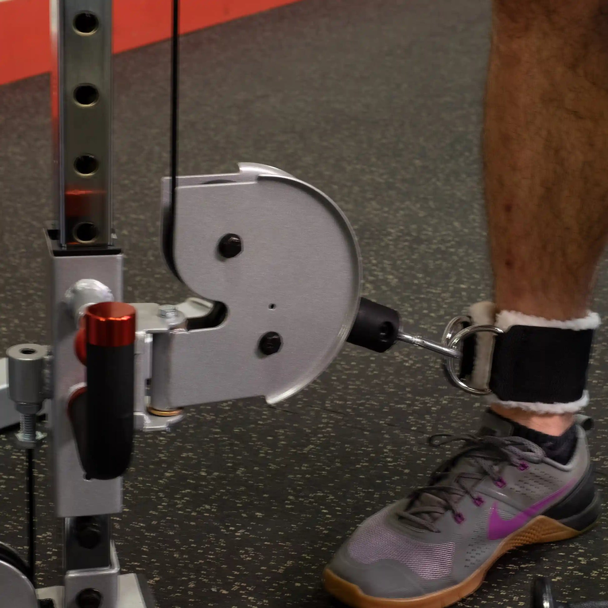Close-up of a Body-Solid Pro ClubLine Series 2 Cable Column S2CC with a leg attachment, featuring a foot in a sneaker secured to the cable system, set against a gym floor.
