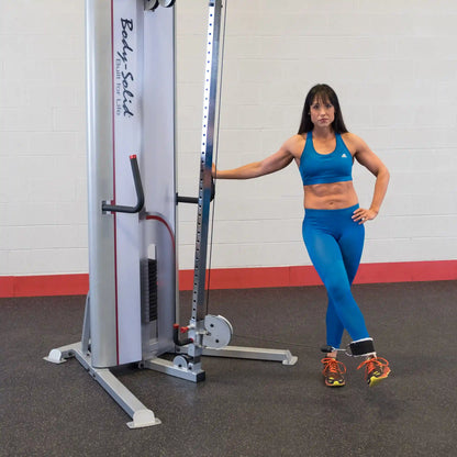 A woman in a blue athletic outfit demonstrating a pose next to the Body-Solid Pro ClubLine Series 2 Cable Crossover S2CCO in a gym setting.