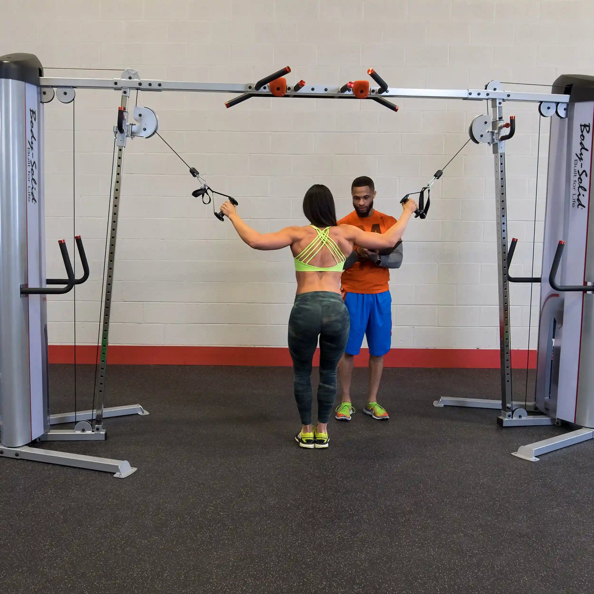 A fitness trainer assists a woman using the Body-Solid Pro ClubLine Series 2 Cable Crossover S2CCO in a gym setting, demonstrating proper form and technique.