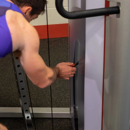 A close-up of a person adjusting the Body-Solid Pro ClubLine Series 2 Cable Crossover S2CCO in a gym setting.