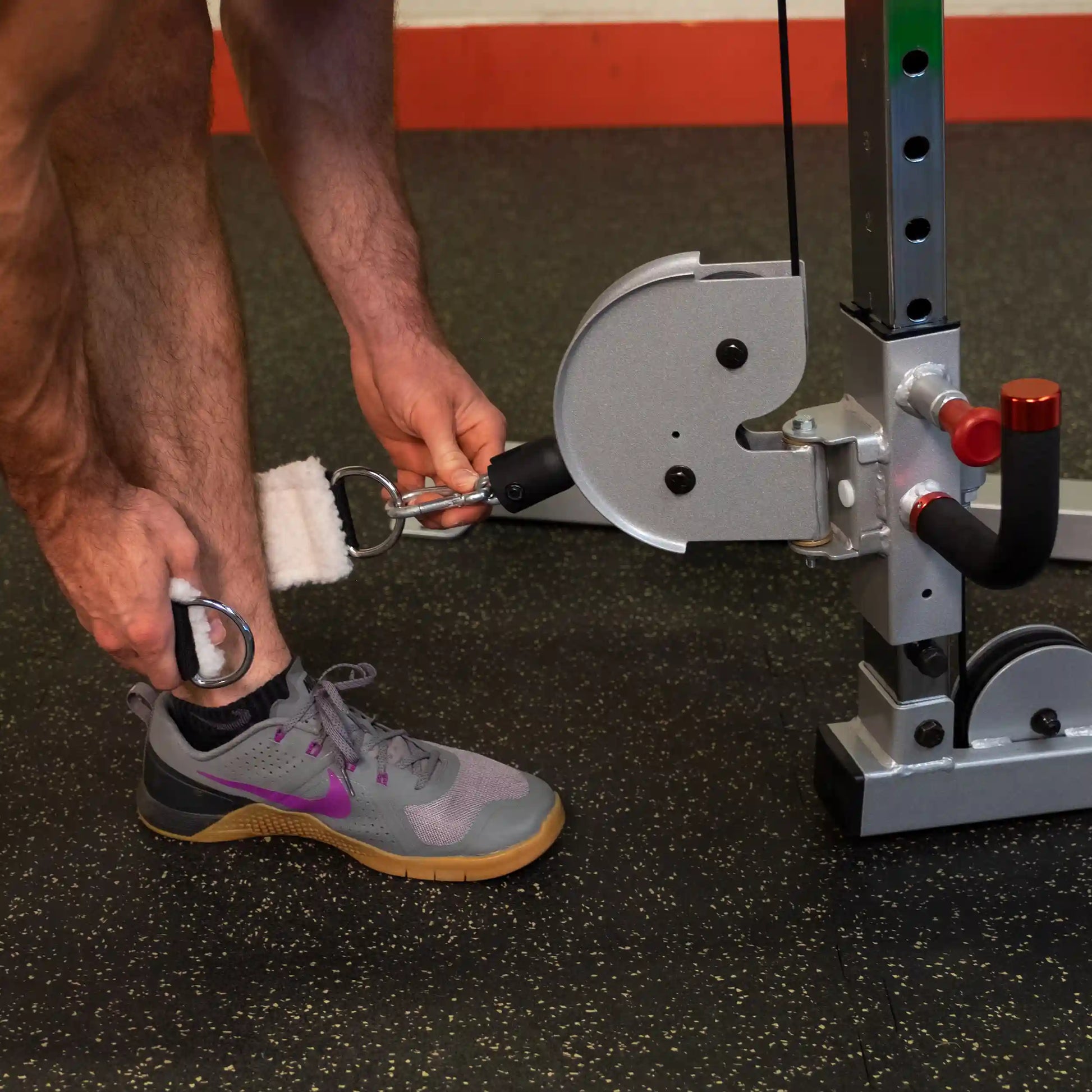 A person adjusts the ankle strap attachment on the Body-Solid Pro ClubLine Series 2 Cable Crossover S2CCO at a gym, demonstrating the equipment's functionality.