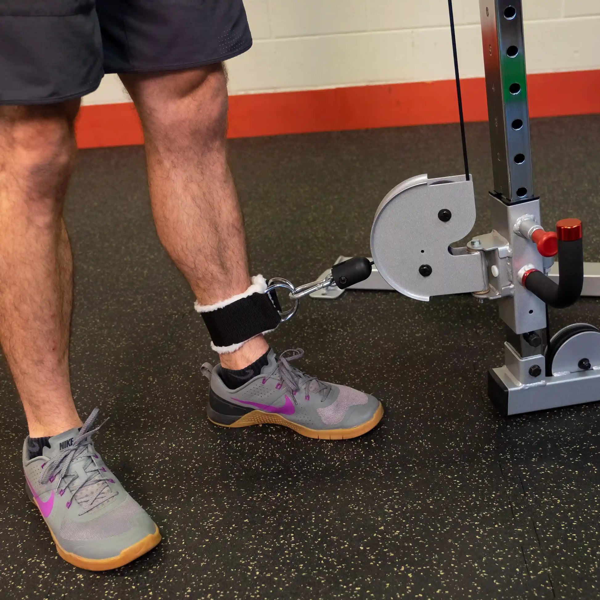 A close-up of a person's leg attached to the Body-Solid Pro ClubLine Series 2 Cable Crossover S2CCO with an ankle strap, demonstrating a cable exercise in a gym setting.