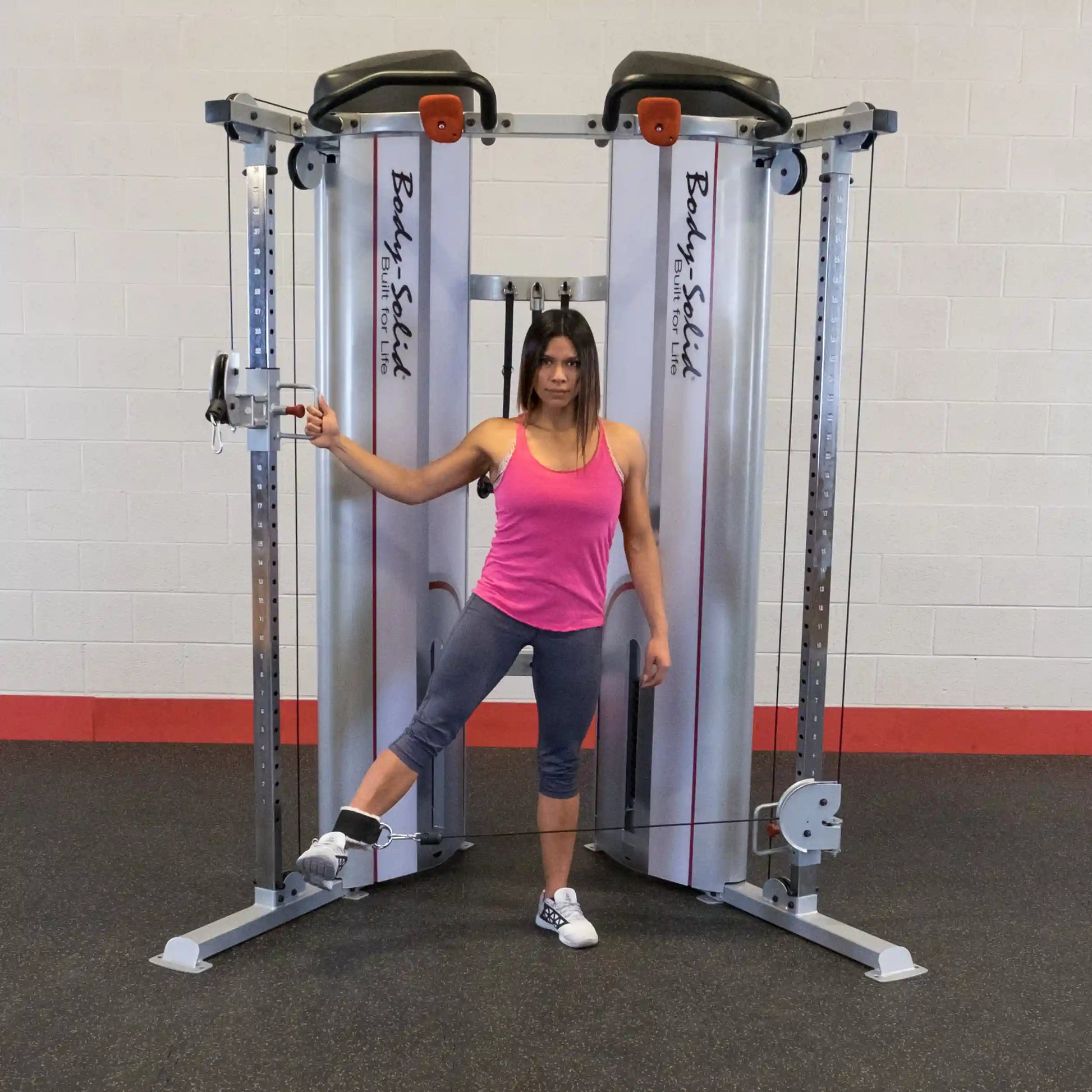 A woman in a pink tank top and gray leggings performing an exercise using the Body-Solid Pro ClubLine Series 2 Functional Trainer S2FT in a gym setting.