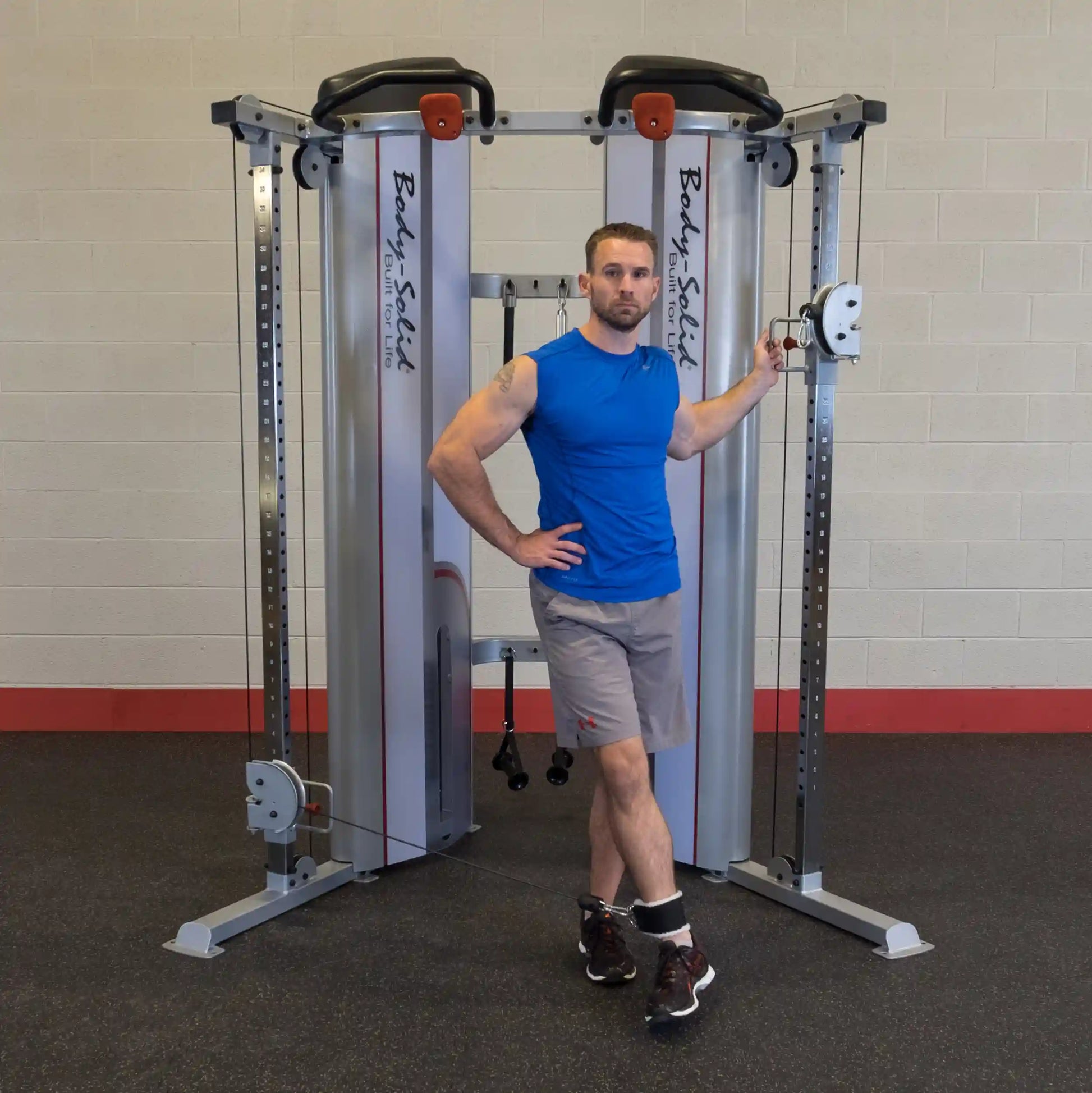 A man in a blue shirt and gray shorts stands next to the Body-Solid Pro ClubLine Series 2 Functional Trainer S2FT, posing with one hand on the equipment.