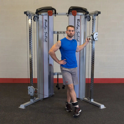 A man in a blue shirt and gray shorts stands next to the Body-Solid Pro ClubLine Series 2 Functional Trainer S2FT, posing with one hand on the equipment.