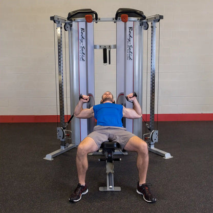 A man performs an exercise on the Body-Solid Pro ClubLine Series 2 Functional Trainer S2FT, lying on a bench with cables in both hands, in a gym setting.