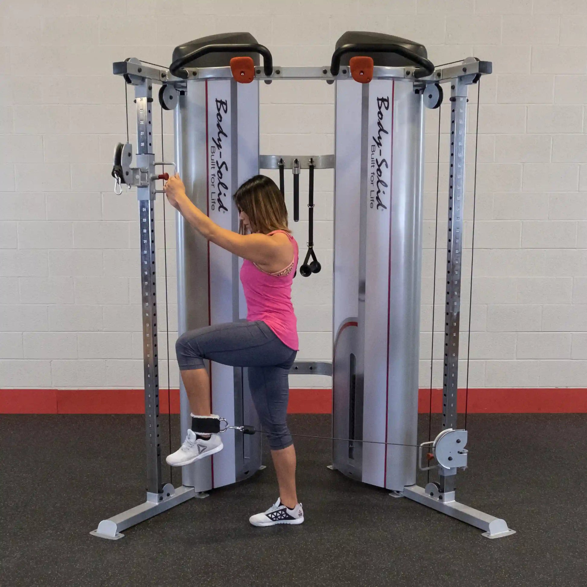 A woman performing an exercise using the Body-Solid Pro ClubLine Series 2 Functional Trainer S2FT, demonstrating a leg lift while attached to the cable machine.