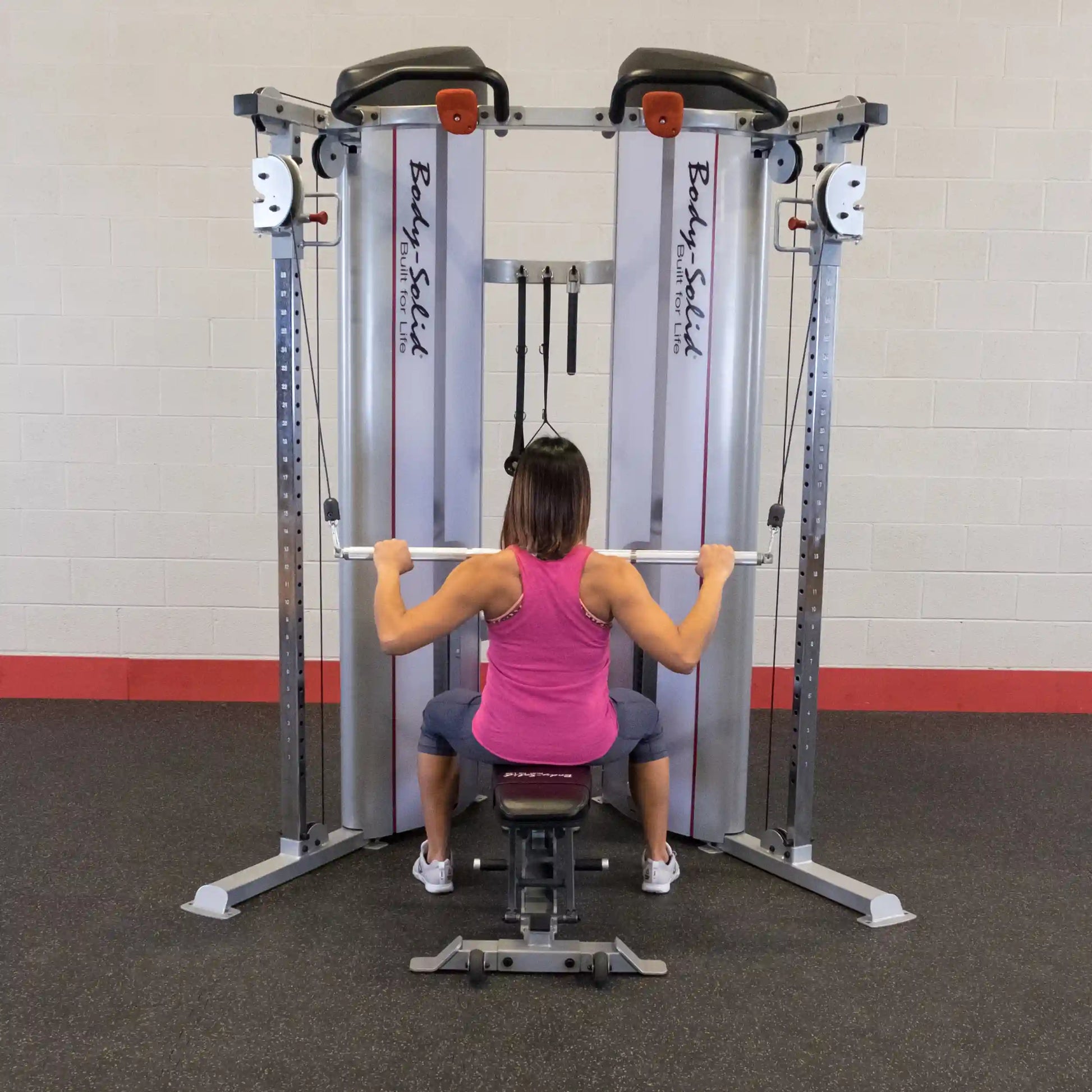 A person using the Body-Solid Pro ClubLine Series 2 Functional Trainer S2FT, seated and pulling on the handles, in a gym setting.