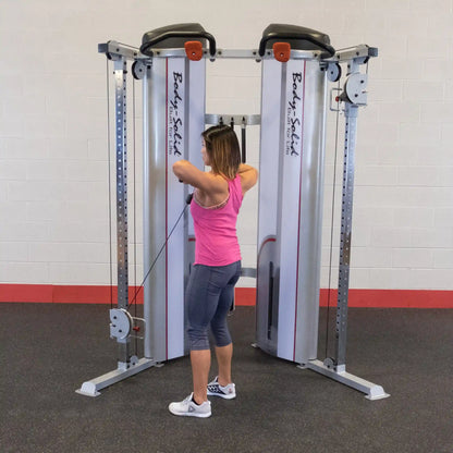 A woman in a pink tank top and gray leggings performs an exercise using the Body-Solid Pro ClubLine Series 2 Functional Trainer S2FT in a gym setting.