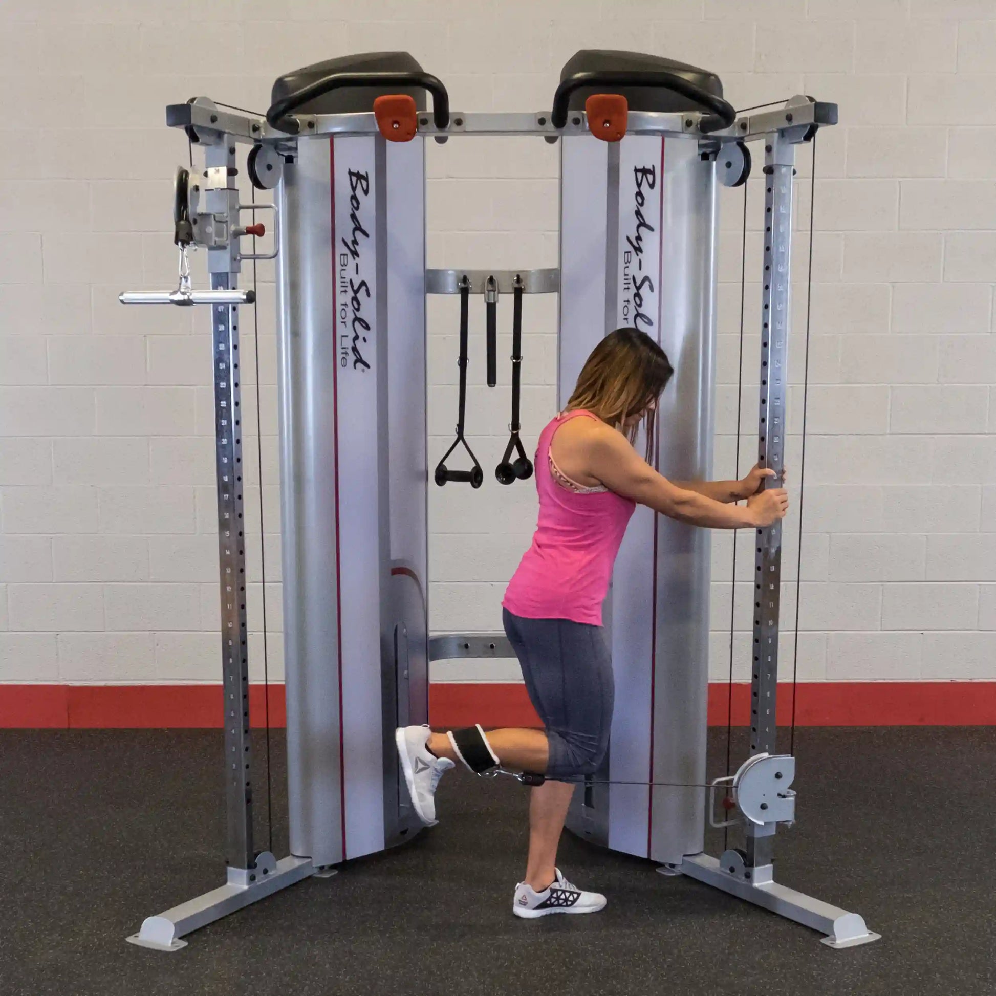 A person using the Body-Solid Pro ClubLine Series 2 Functional Trainer S2FT for leg exercises, demonstrating proper form while standing beside the equipment.