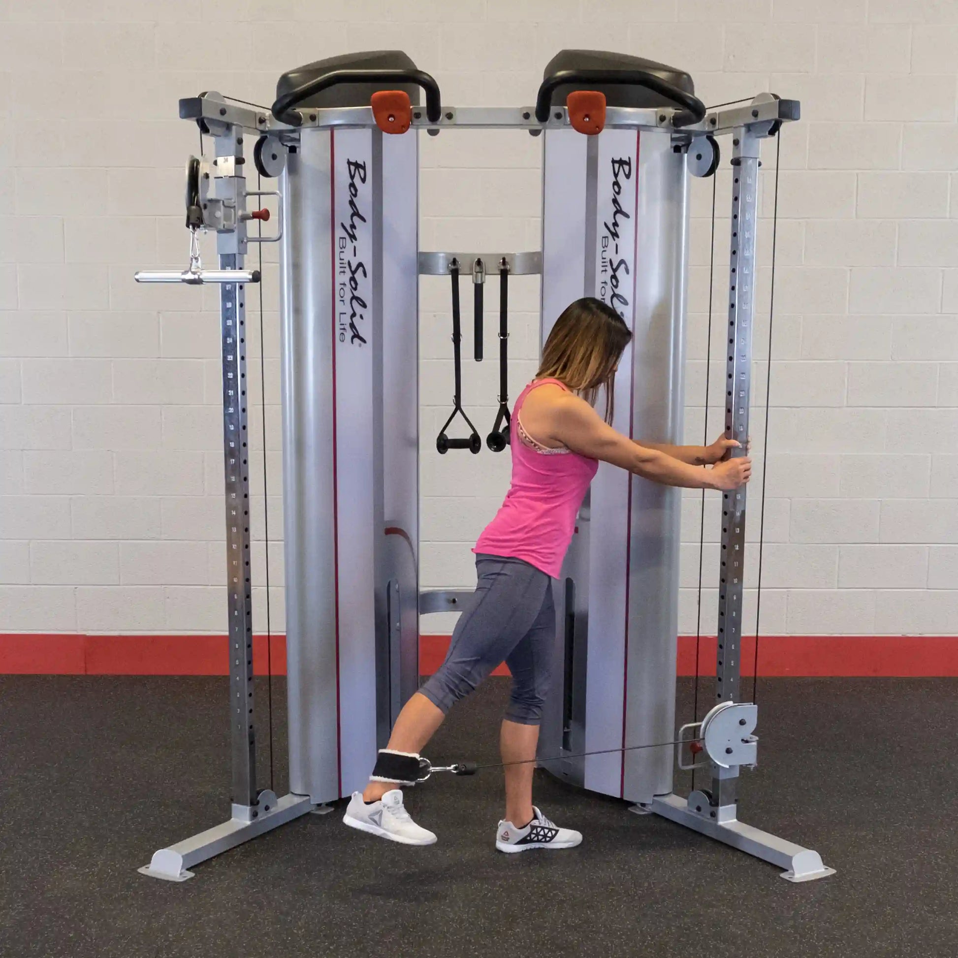 A woman using the Body-Solid Pro ClubLine Series 2 Functional Trainer S2FT, performing an exercise with one leg attached to the cable machine, in a gym setting.