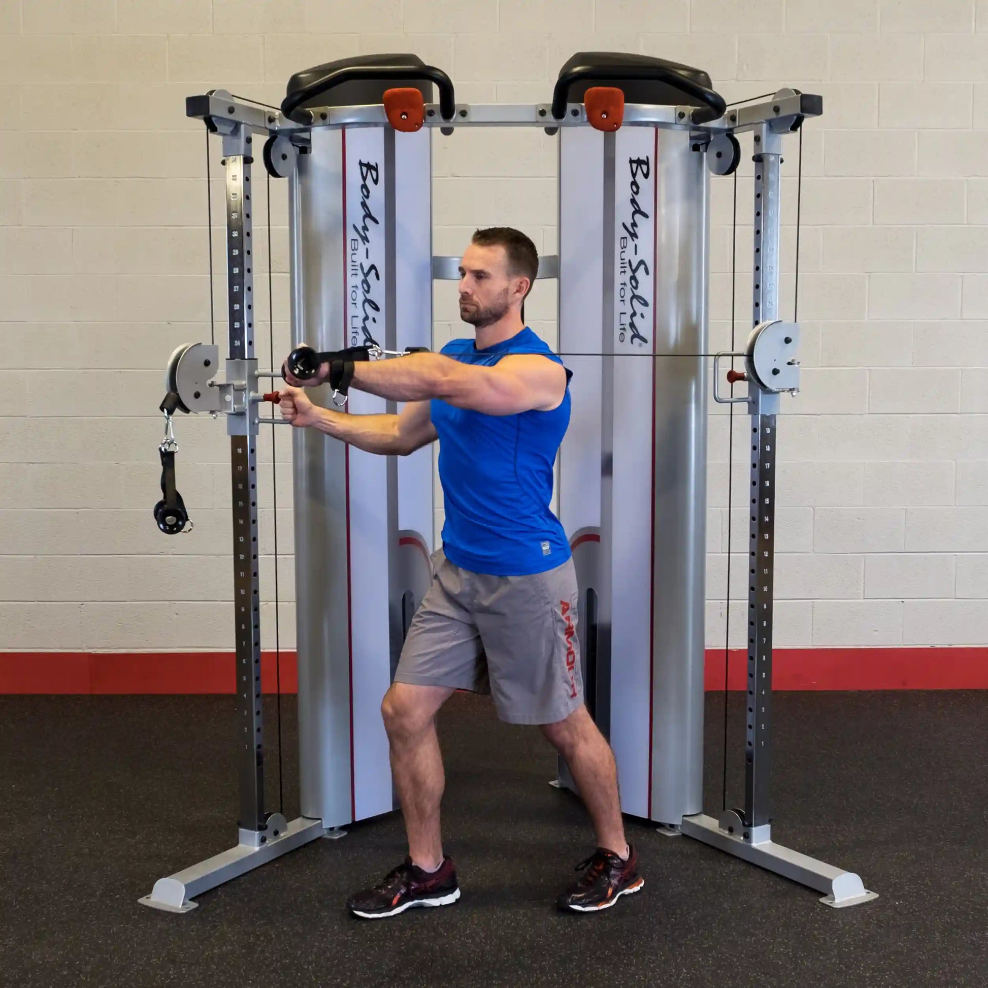 A person demonstrating an exercise using the Body-Solid Pro ClubLine Series 2 Functional Trainer S2FT, with one arm extended forward while holding a handle. The gym setting features gray walls and a black floor.